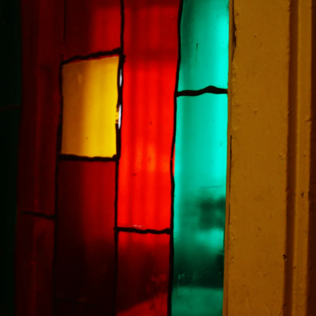 Fragmento de una vidriera emplomada a contraluz, con vidrios rojos, amarillos y verdes separados por perfiles de plomo oscuros.